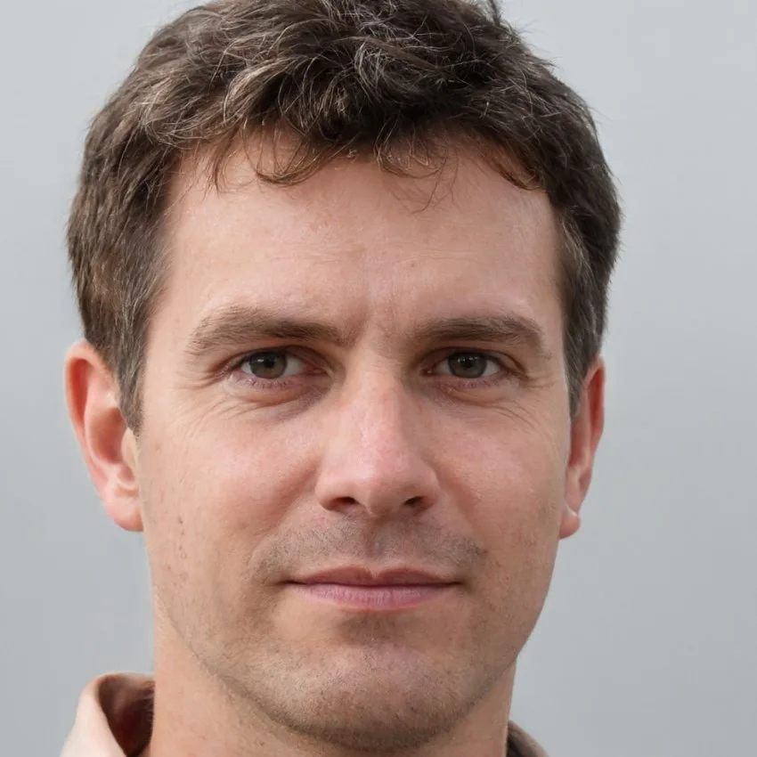 Portrait of John Peterson, a professional with short brown hair, wearing a neutral expression and a beige collared shirt, set against a plain gray background.